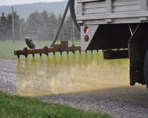 A closeup of a Dustkill truck distributing treatment formula to a gravel road.